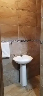 a bathroom with a white sink and brown tiles at Whitehouse Lodge Benoni in Benoni