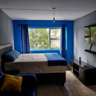 a bedroom with blue walls and a bed and a window at Greggs Place at Capital Hill Arcadia in Pretoria