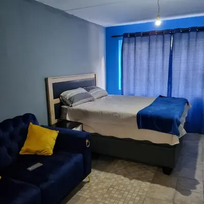 a blue bedroom with a bed and a couch at Greggs Place at Capital Hill Arcadia in Pretoria