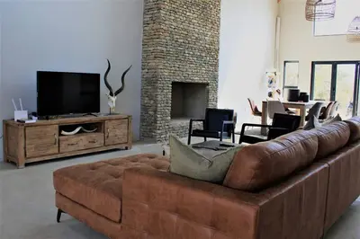 a living room with a brown couch and a television at Ebony House - Kruger National Park in Hectorspruit