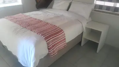 a white bed with a pink blanket and a side table at Mandy place in Sandown