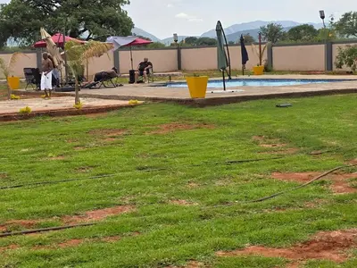 a yard with grass and a pool with umbrellas at KGADITSE ROAD LODGE in Moletlane