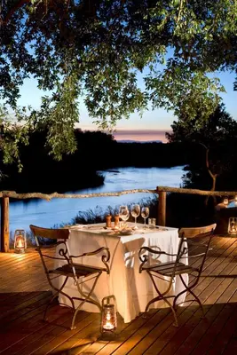 a table with wine glasses on a deck with a lake at Lion Sands - Tinga Lodge in Skukuza