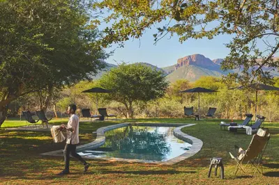 a man walking by a pool with a mountain in the background at Marataba Safari Lodge in Hartbeestfontein