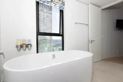 a white bathroom with a tub and a window at The Executive Apartment in Ellipse Waterfall City in Midrand