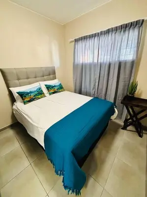 a bedroom with a bed with a blue blanket and a window at The Place at Mall of Africa 2 in Midrand