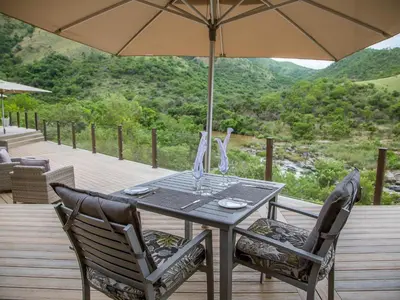 a table with two chairs and an umbrella on a deck at Nkomazi Game Reserve by NEWMARK in Badplaas