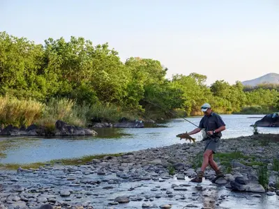 a man is standing on a river holding a fishing rod at Nkomazi Game Reserve by NEWMARK in Badplaas