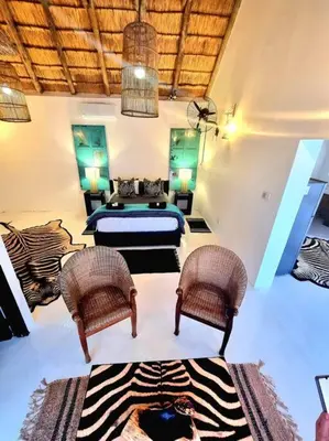 a bedroom with a bed and two wicker chairs at Luxury GuesthouseCo RomanticaHouse in Marloth Park