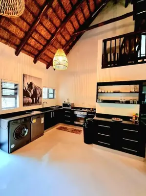 a large kitchen with black cabinets and a chandelier at Luxury GuesthouseCo FarmHouse in Marloth Park