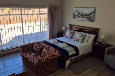 a bedroom with a bed and a chair and a window at Hornbill Helipad 2 in Centurion