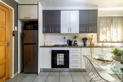 a kitchen with white cabinets and a glass table at Cheerful Cottage in Johannesburg