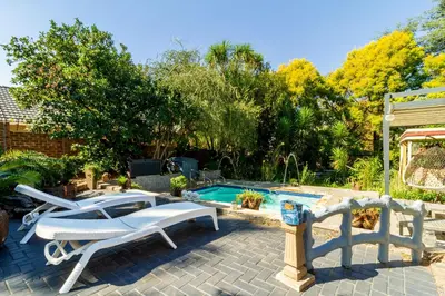 a backyard with a pool and two lounge chairs and a swimming pool at Cheerful Cottage in Johannesburg