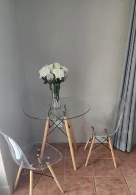 a glass table with a vase of flowers and two chairs at Tswenyane Kruger Riverview Apartments in Marloth Park