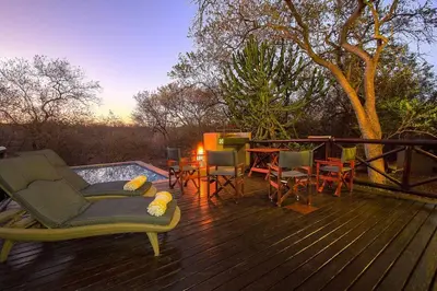 a deck with chairs and a table and a pool at Luxury GuesthouseCo HoneymoonHouse in Marloth Park
