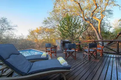 a deck with a pool and chairs and a table at Luxury GuesthouseCo HoneymoonHouse in Marloth Park