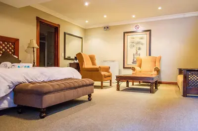 a bedroom with a bed and two chairs and a table at RIETONDALE LODGE in Pretoria