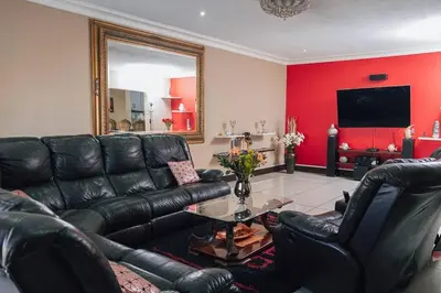 a living room with black leather furniture and a red wall at Ray of sunshine in Centurion