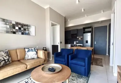 a living room with a couch and blue chairs and a table at Capital Trilogy Apartments in Pretoria