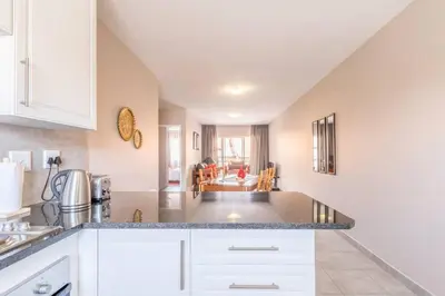 a kitchen with white cabinets and a living room at NO loadshedding 3km to Gautrain Short or Long stays Uncapped Wi-Fi in Centurion