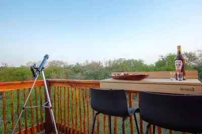 a microphone and two chairs on a deck with a bottle of beer at The Suite Luxury Safari Villa, Close to KNP, Starbed, Giraffe-Feeding-Tower, Bush-Bath in Marloth Park