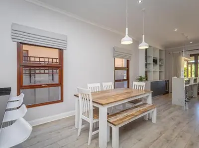 a dining room with a wooden table and white chairs at Golf & Leisure Delight - Pecanwood Golf Estate - Hartbeespoort in Hartbeespoort