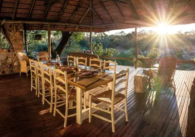 a wooden table and chairs on a deck with the sun at Motswari African Retreat & Walking Safaris by NEWMARK in Timbavati Game Reserve