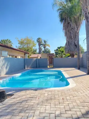 a swimming pool in a backyard with a fence and palm trees at Divine Sleep in Bela-Bela