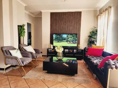 a living room with a couch and chairs and a tv at Lions Haven in Pretoria