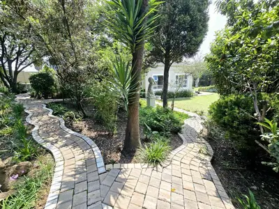 a brick walkway in a garden with a palm tree at Waterfall City Guest Lodge in Sandton