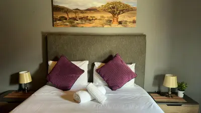 a bedroom with a bed with purple pillows and a painting at K K K Guesthouse in Secunda