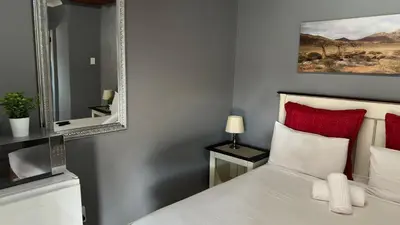 a bedroom with a white bed with red pillows and a mirror at K K K Guesthouse in Secunda
