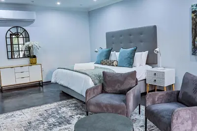 a bedroom with a bed with blue walls and two chairs at Siesta Manor Guesthouse in Mokopane
