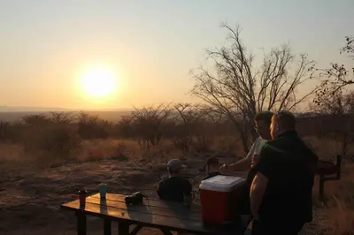 a group of people standing around a bench with the sunset at The Sanctuary in Mabalingwe Nature Reserve in Mabula
