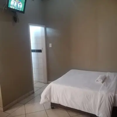 a bedroom with a white bed and a television at Ebony Guest House in Pretoria