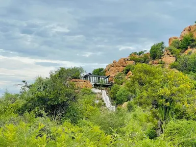 a house on the side of a hill with trees at Makgobelo Lodge-The Glass House- Solar powered in Ga-Mokalapa