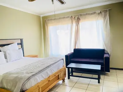 a bedroom with a bed and a chair and a window at c and c guest house pretoria north in Pretoria