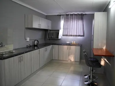 a kitchen with white cabinets and a sink and a chair at Aqua Guest House in Sandown