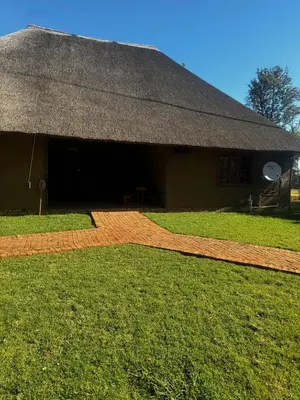 a building with a straw roof and a grass yard at Falcon Lodge Bela Bela in Merinovlakte
