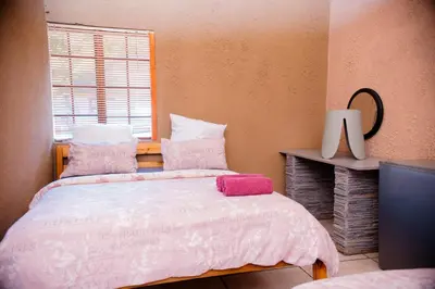 a bedroom with a bed with pink sheets and a window at Falcon Lodge Bela Bela in Merinovlakte