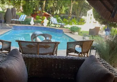 a swimming pool with wicker chairs and a swimming pool at The Giraffe Room at Frederick's Place in Pretoria