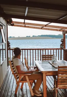 a woman sitting at a table on the deck of a boat at Die Boothuis at Lake Chrissie in Lake Chrissie