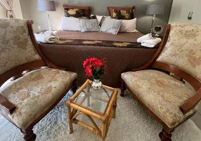 a bedroom with a bed with two chairs and a table with flowers at The Presidential Suite at Frederick's Place in Pretoria