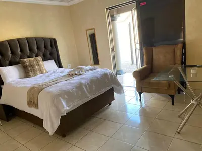 a bedroom with a bed and a chair and a glass table at Whizzy Lifestyle Lodge in Witbank