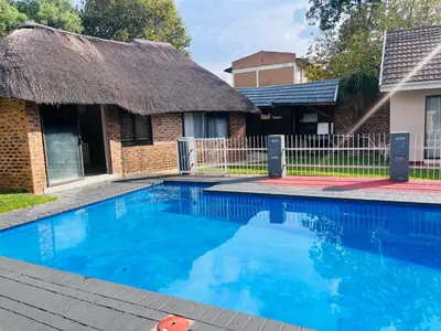 a swimming pool in front of a house with a thatch roof at Eccoo OR Tambo Airport lodge in Kempton Park