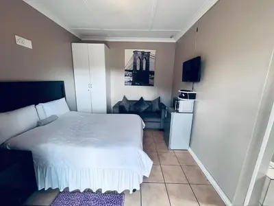 a bedroom with a white bed and a refrigerator at Eccoo OR Tambo Airport lodge in Kempton Park