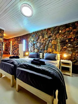 a bedroom with two beds in front of a stone wall at Luxury GuesthouseCo FlintstoneHouse in Marloth Park