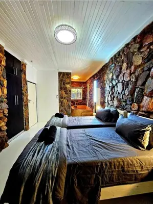 a bedroom with two beds and a stone wall at Luxury GuesthouseCo FlintstoneHouse in Marloth Park
