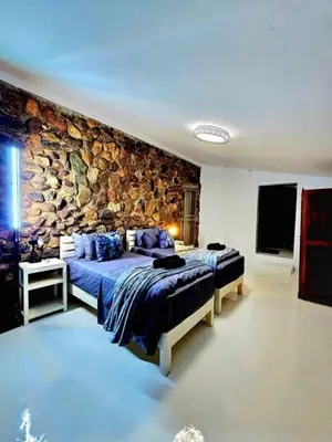 a bedroom with two beds and a stone wall at Luxury GuesthouseCo FlintstoneHouse in Marloth Park