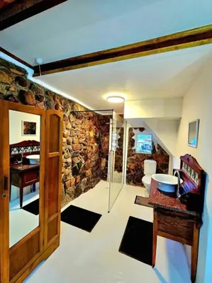 a room with a bathroom with a stone wall at Luxury GuesthouseCo FlintstoneHouse in Marloth Park